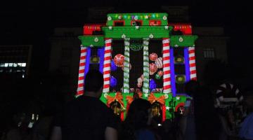 pessoas assistindo a projeção mapeada #paratodosverem
