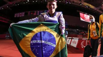 Nathan segura a bandeira do brasil na frente do corpo. Ele está dentro da arena. #paratodosverem