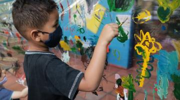 Criança pintando mural de plástico #paratodosverem
