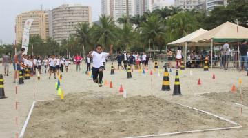 criança saltando na areia e várias assistindo ao fundo na praia #paratodosverem