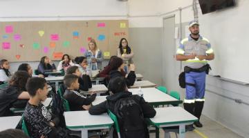 agente de trânsito está à frente de lousa em sala de aula e alunos estão assistindo. #paratodosverem