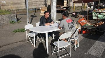 Em uma mesa na rua, homem recebe atendimento #paratodosverem