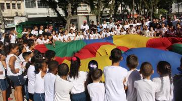 Crianças erguem tecido colorido em movimento conjunto. #paratodosverem