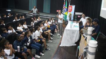 crianças estão sentadas em auditório assistindo palestra. #paratodosverem