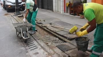 homens estão aplicando concreto em meio fio, ao lado de grelhas. #paratodosverem