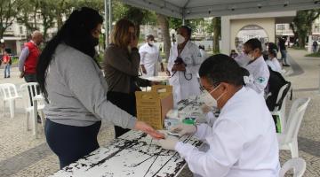 mulher faz teste de glicemia em estande com várias pessoas na praça #paratodosverem