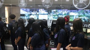 jovens todos de costas para a foto olham para sala de monitoramento do Centro de Controle Operacional. #paratodosverem