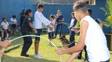 crianças seguram bambolês para cachorro passar entre eles. #paratodosverem