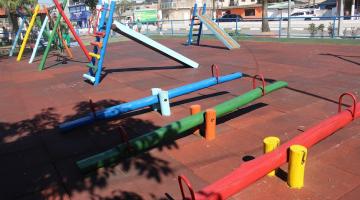 playground com gangorras em primeiro plano e escorregadores ao fundo. #paratodosverem 