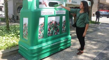 mulher coloca garrafa de vidro dentro de recipiente em praça. #paratodosverem