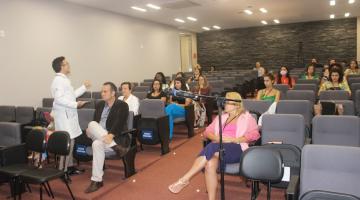 pessoas estão sentadas em auditório assistindo a uma palestra. Homem está em pé falando a todos. #paratodosverem 