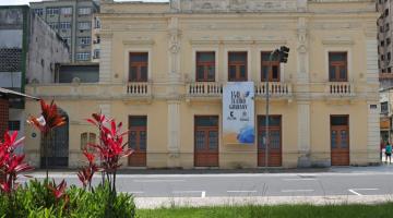 a fachada do teatro coliseu, com flores em uma praça (à esq.) em primeiro plano. #paratodosverem 