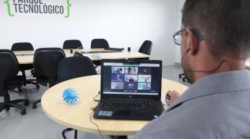 homem está de costas para a foto e diante de um monitor de computador que está sobre uma mesa. Ao lado do monitor, um pequeno protótipo de gerador de energia.  #paratodosverem