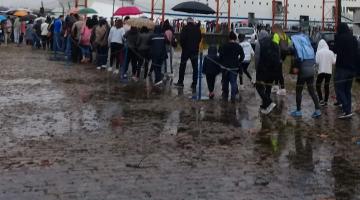 Fila de pessoas no cais para entrar no navio. Dia está chuvoso. 