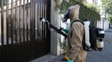 Homem paramentado com macacão, máscara e equipamento nebulizador nas costas. #Paratodosverem