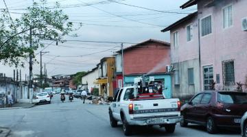 carro com equipamento de dispersão de produto na caçamba passa por rua. #paratodosverem