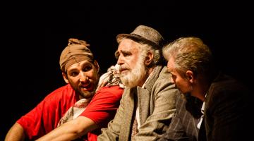 Homens sentados conversam em cena teatral #paratodosverem