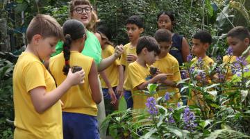 mulher orienta crianças em jardim florido. #paratodosverem
