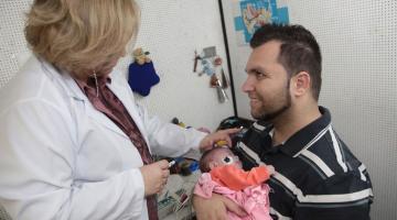 médica atende bebê no colo de um homem . #paratodosverem