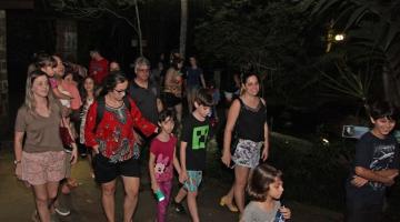 vários adultos e crianças caminhando por alameda do orquidário à noite. #paratodosverem