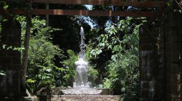 a entrada do orquidário, com vegetação nas laterais e a estátua da ninfa náiade ao centro e ao fundo. #paratodosverem