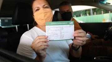 mulher dentro de carro sorri segurando comprovante de vacinação. #paratodosverem