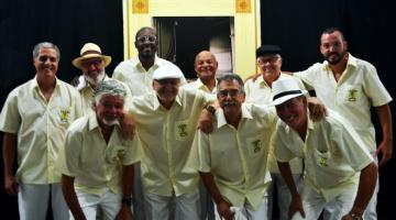 Integrantes da roda de samba ouro verde posam para foto. Todos usam camisa amarela e calça branca. #paratodosverem
