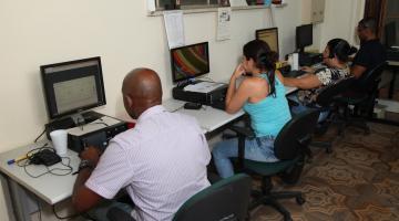 Agentes da ouvidoria sentados e de frente para tela de computador. #Paratodosverem