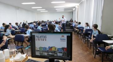 Computador com tela sobre projeto e crianças e prefeito ao fundo #paratodosverem
