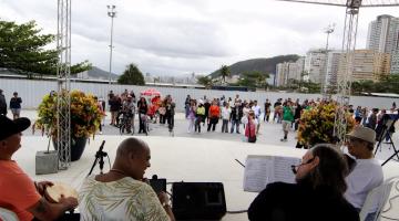 músicos tocam em palco e público está ao fundo. #paratodosverem