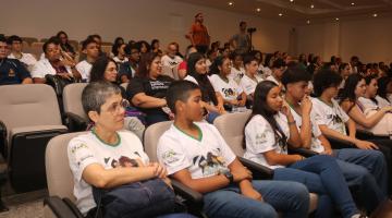 alunos uniformizados sentados em auditório. #paratodosverem 