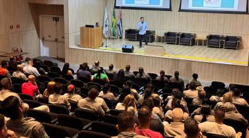 auditório lotado de pessoas assistindo palestra de uma pessoa no palco. Há telões com mensagens ao fundo. #paratodosverem 