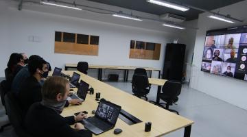 Pessoas estão sentadas diante de seus laptops aberto e assistindo a uma apresentação em telão. #paratodosverem