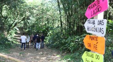pessoas caminham por trilha sinalizada por placas. #paratodosverem