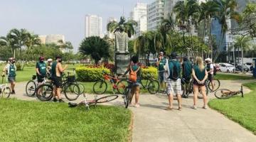 Pessoas de bicicleta ao redor de monumento na orla da praia #paratodosverem