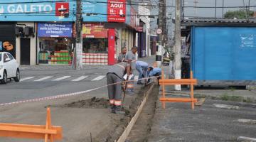 Trecho está delimitado por cavalete e fita. Operários está manuseando enxadas junto à guia. #Paratodosverem