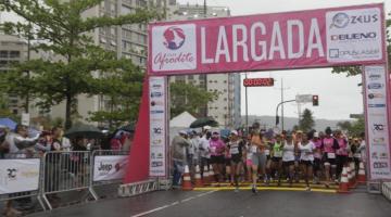 Atletas embaixo do portal escrito Largada com prédios ao fundo. #paratodosverem