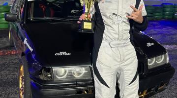 Imagem do piloto com o carro e troféu. #Paratodosverem.