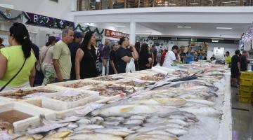 pessoas olham peixes expostos no mercado #paratodosverem 