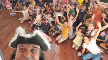 pirata em primeiro plano fazendo selfie com várias crianças ao fundo com os braços para cima. #paratodosverem 