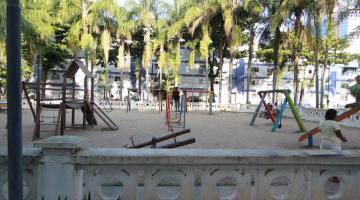 área de playground com brinquedos sobre piso de areia. À frente, o cercado é feito com as tradicionais muretas de santos. #paratodosverem