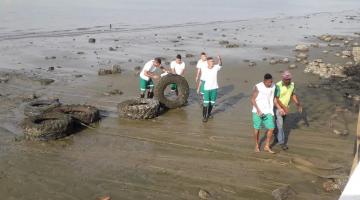 operários estão na faixa de areia mexendo e juntando pneus. #paratodosverem