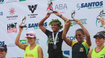 Pódio feminino com Ivanilda Pereira dos Santos ao centro. Elas estão todas com os braços para o alto segurando os troféus. #paratodosverem