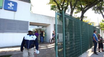 Homem sai da unidade de saúde e passa por portão. #paratodosverem
