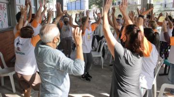 pessoas fazem movimento de alongamento em pé. #paratodosverem