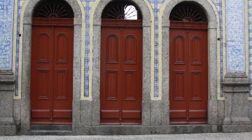 três portas na entrada de uma única edificação azulejada. #paratodosverem