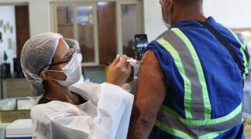 mulher vacina homem com roupa de operario e faixa reflexiva no uniforme. #paratodosverem