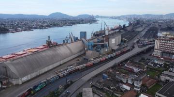vista geral de área da cidade adjacente ao porto, com armazens, linha férrea, avenidas e construções do lado direito. O mar e a margem esquerda (guarujá) estão à esquerda. #paratodosverem