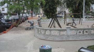 dois homens trabalham na obra de praça. A calçada tem árvores e o entorno da praça tem as tradicionais muretas da Cidade. #paratodosverem