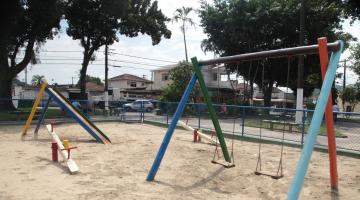 Play ground em praça, com conjunto de dois balancês, uma gangorra e um escorregador. #Paratodosverem